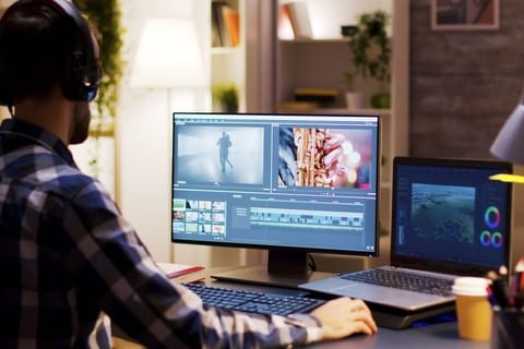 Content creator wearing a headset working on a desktop and laptop — representing video editing and multitasking workflows